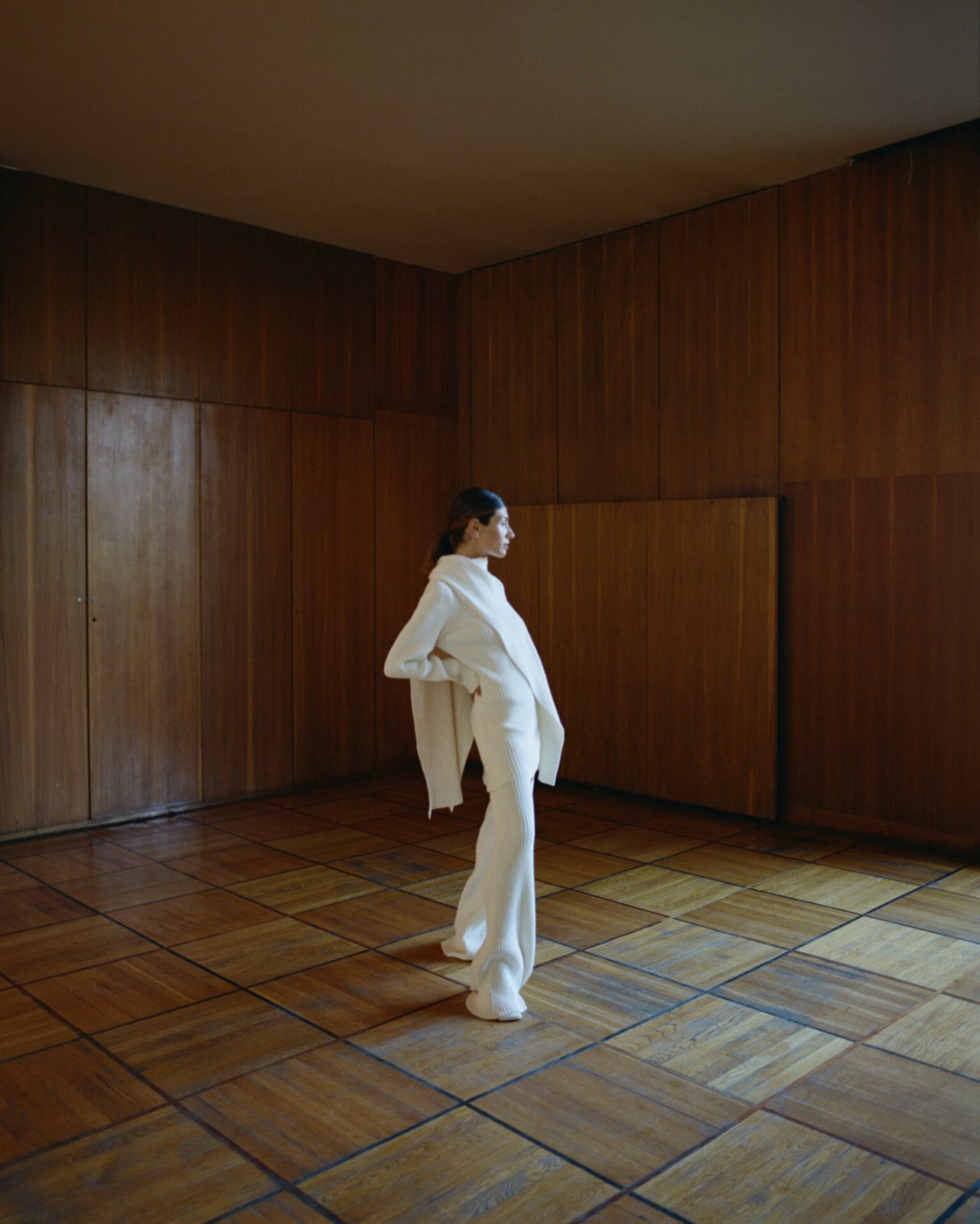 COS — profile in a dark green coat against a white wall with leaf shadows