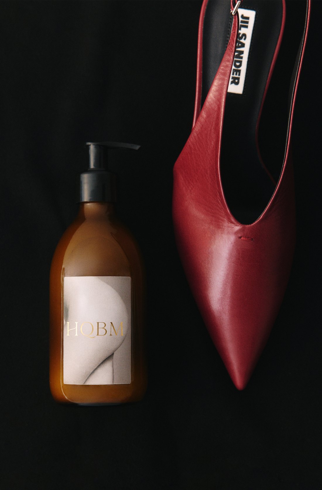 HQBM — still life, the brand bottle beside a burgundy Jil Sander slingback on black