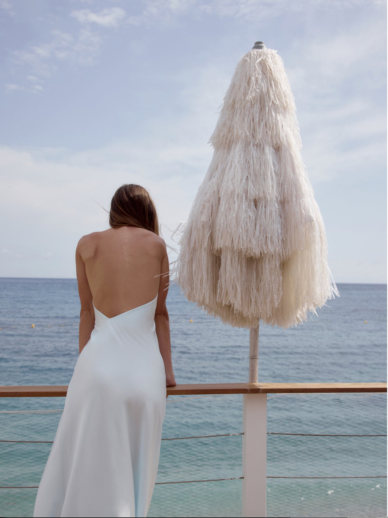 MIOGI LI — campaign, white satin dress by the sea beside a raffia parasol