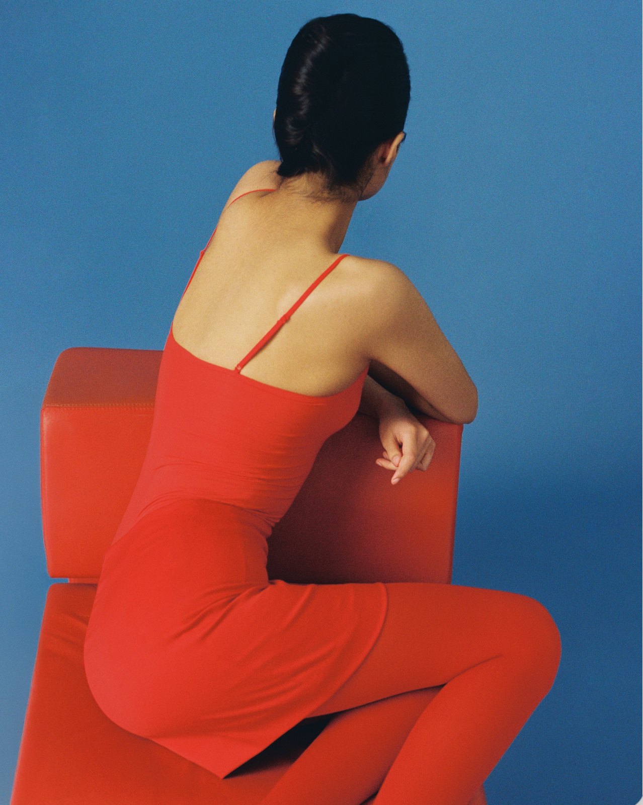 Editorial — figure in red seated on a red chair against blue