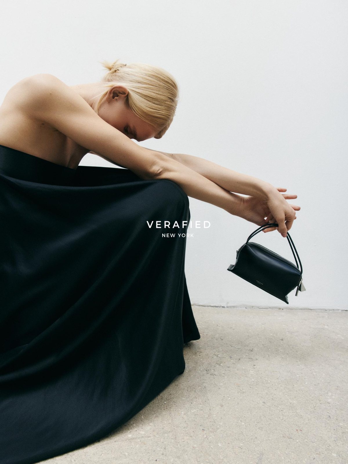 VERAFIED New York — seated figure in a black gown holding a mini bag